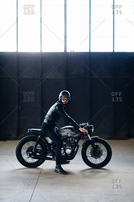 Young male motorcyclist on vintage motorcycle in empty warehouse, portrait