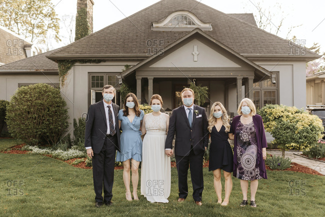 Wedding party posing for group portrait on front lawn, wearing face masks during Coronavirus crises.