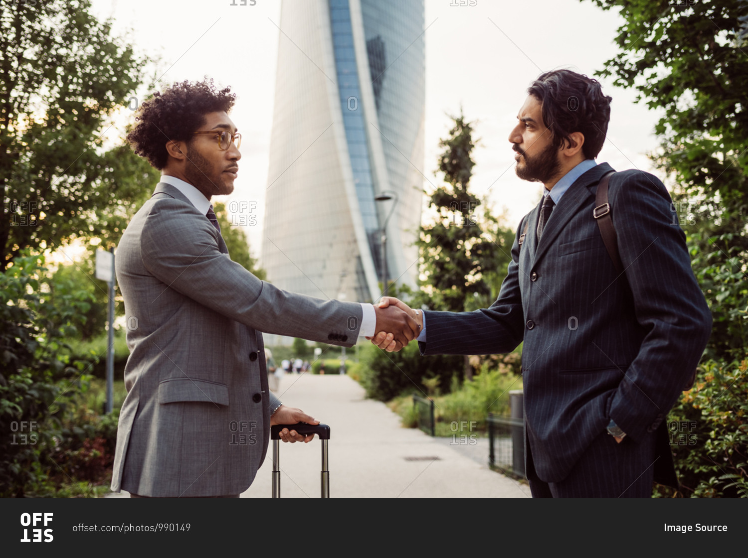Two businessmen wearing suits standing outdoors, shaking hands.