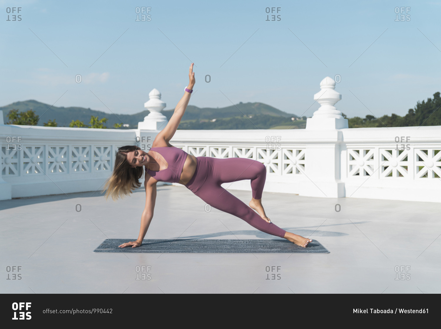 Young woman practicing side plank pose on building terrace against sky
