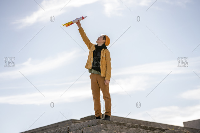 Boy holding rocket toy while standing on steps against sky