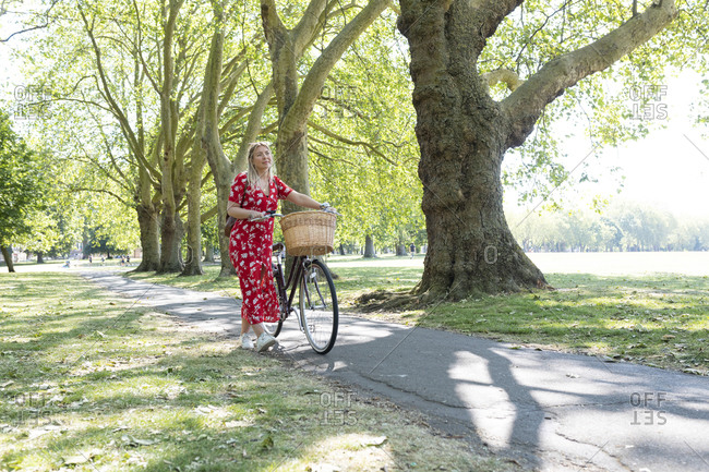 Thoughtful woman walking with bicycle on footpath in public park