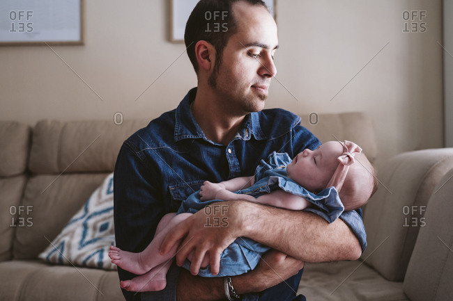 Father carrying sleeping baby girl on sofa at home