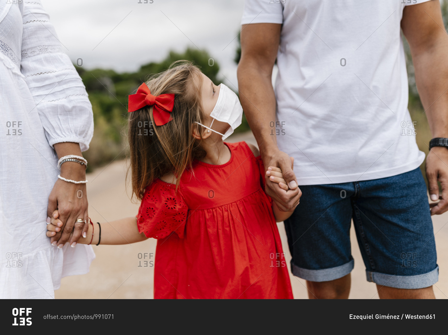 Girl wearing mask looking at father while holding hands on country road