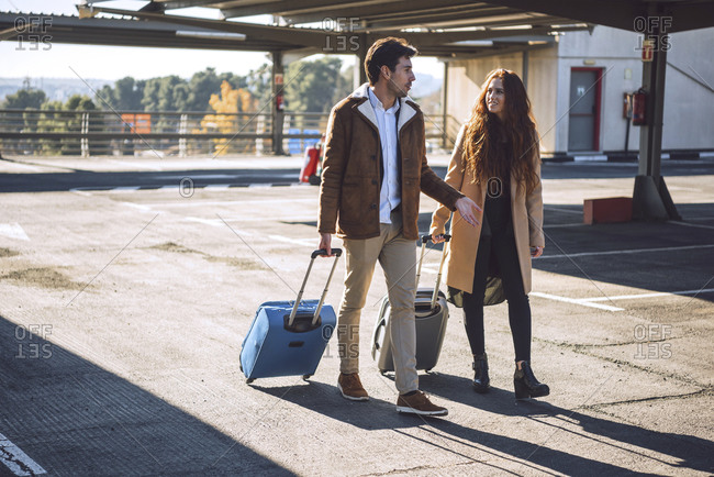 Business couple pulling luggage while walking at airport parking lot