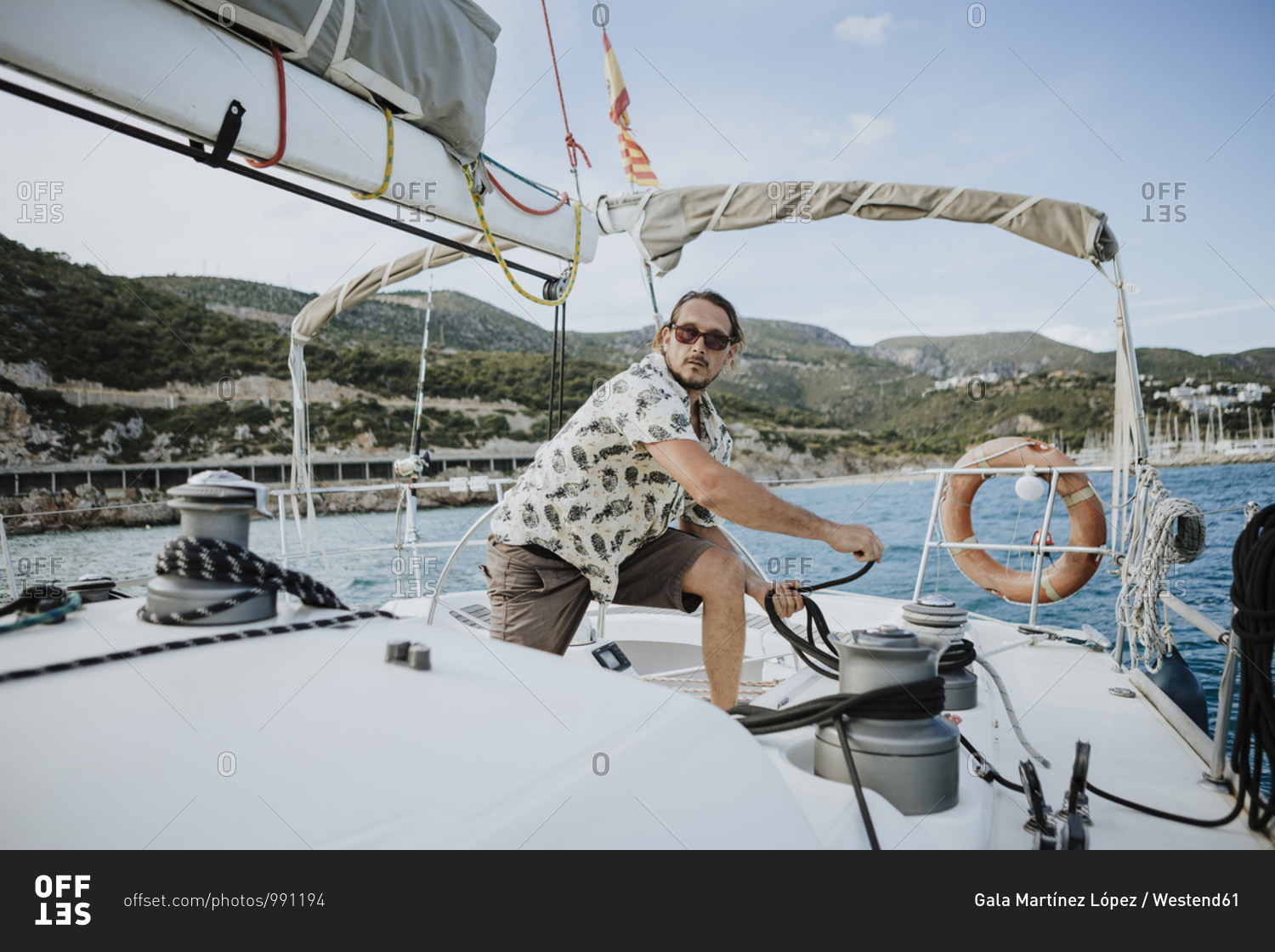 Male sailor maneuvering with winch in sailboat against sky
