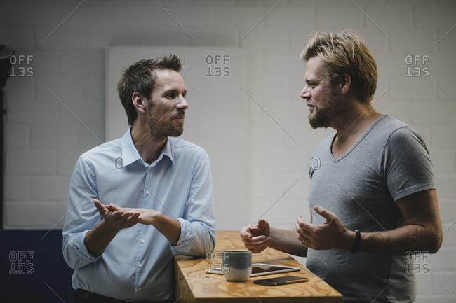 Two casual businessmen discussing in office with portable devices on counter