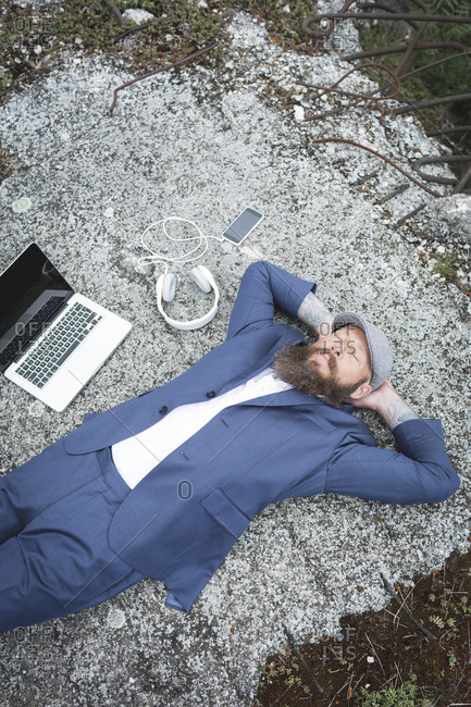 Bearded businessman with hands behind head relaxing on land in forest
