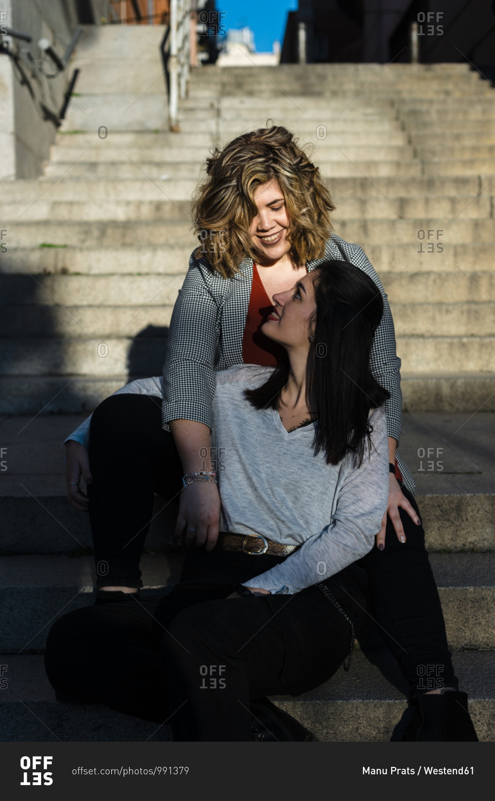 Lesbian couple looking at each other while sitting on steps in city