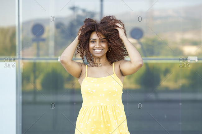 Happy young woman with hair in hair wearing yellow dress standing against wall