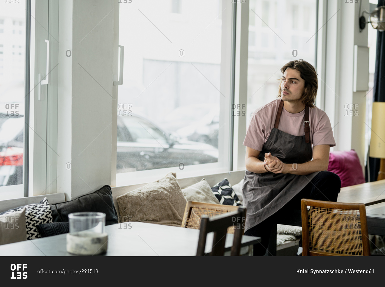 Thoughtful barista with hands clasped sitting on table in cafe