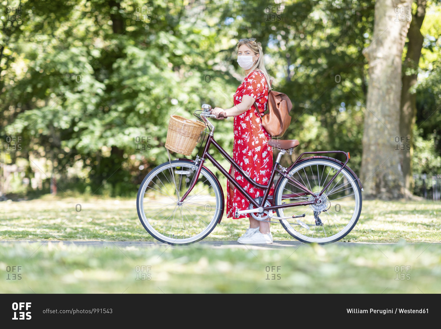 Woman wearing mask while standing with bicycle on footpath in park