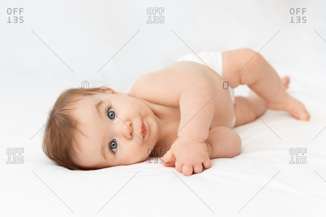 Cute baby with funny expression lying the side on white bed