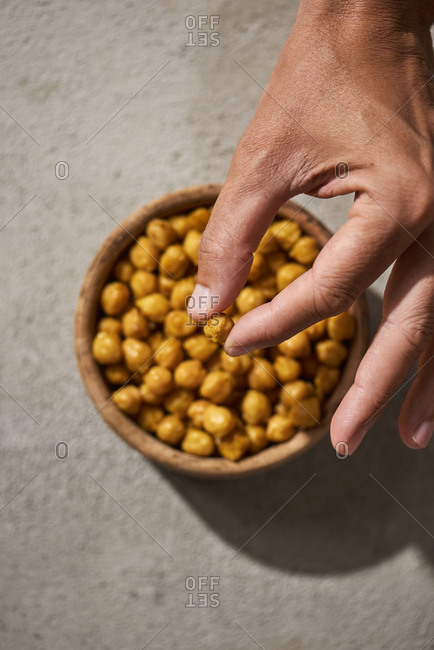 High angle view of a man taking a cooked chickpea, seasoned with curry powder, from a wooden bowl placed on a rustic gray surface