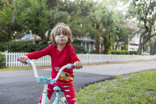 A five year old boy in a red shirt riding his bike on a quiet residential street.