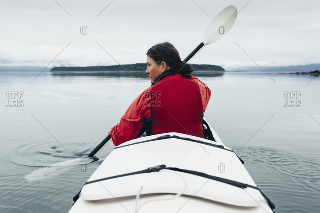 A middle-aged woman paddles sea kayak in the pristine waters of Muir Inlet, Glacier Bay National Park and Preserve, Alaska