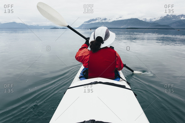 A middle-aged woman paddles sea kayak in the pristine waters of Muir Inlet, Glacier Bay National Park and Preserve, Alaska