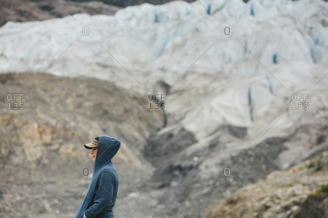 A young woman standing at the end of a glacier on a rocky shoreline in Alaska.