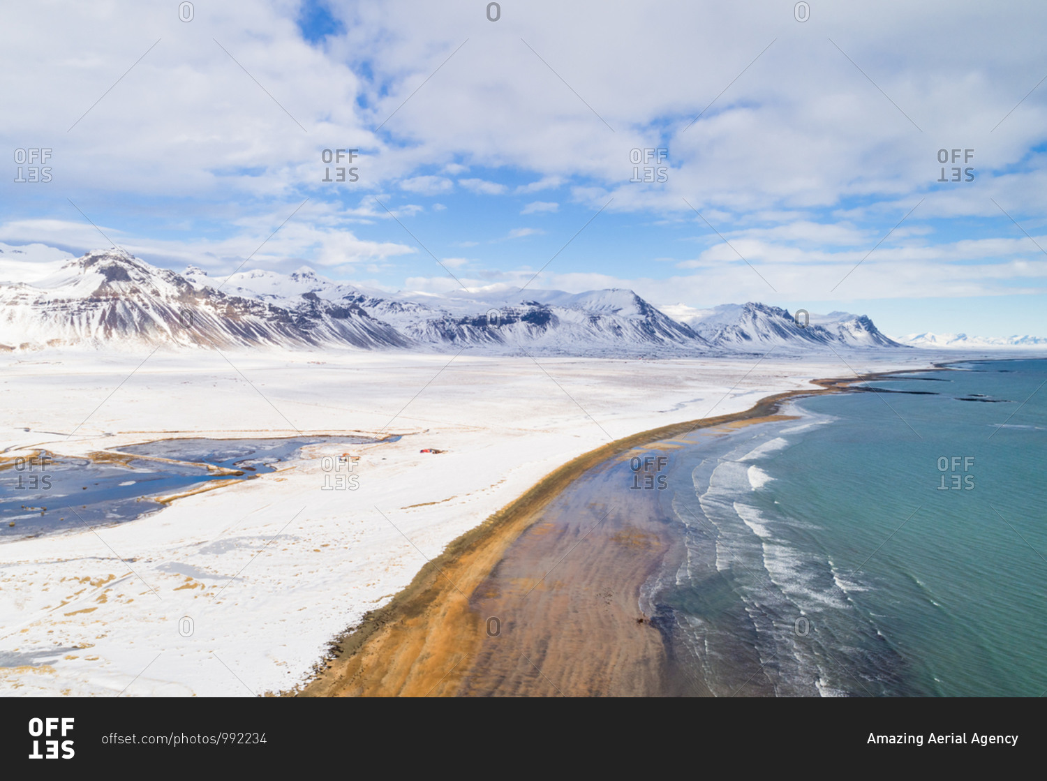 Aerial view of beach along land and mountains covered with snow during winter in Snaefellsnes, Iceland