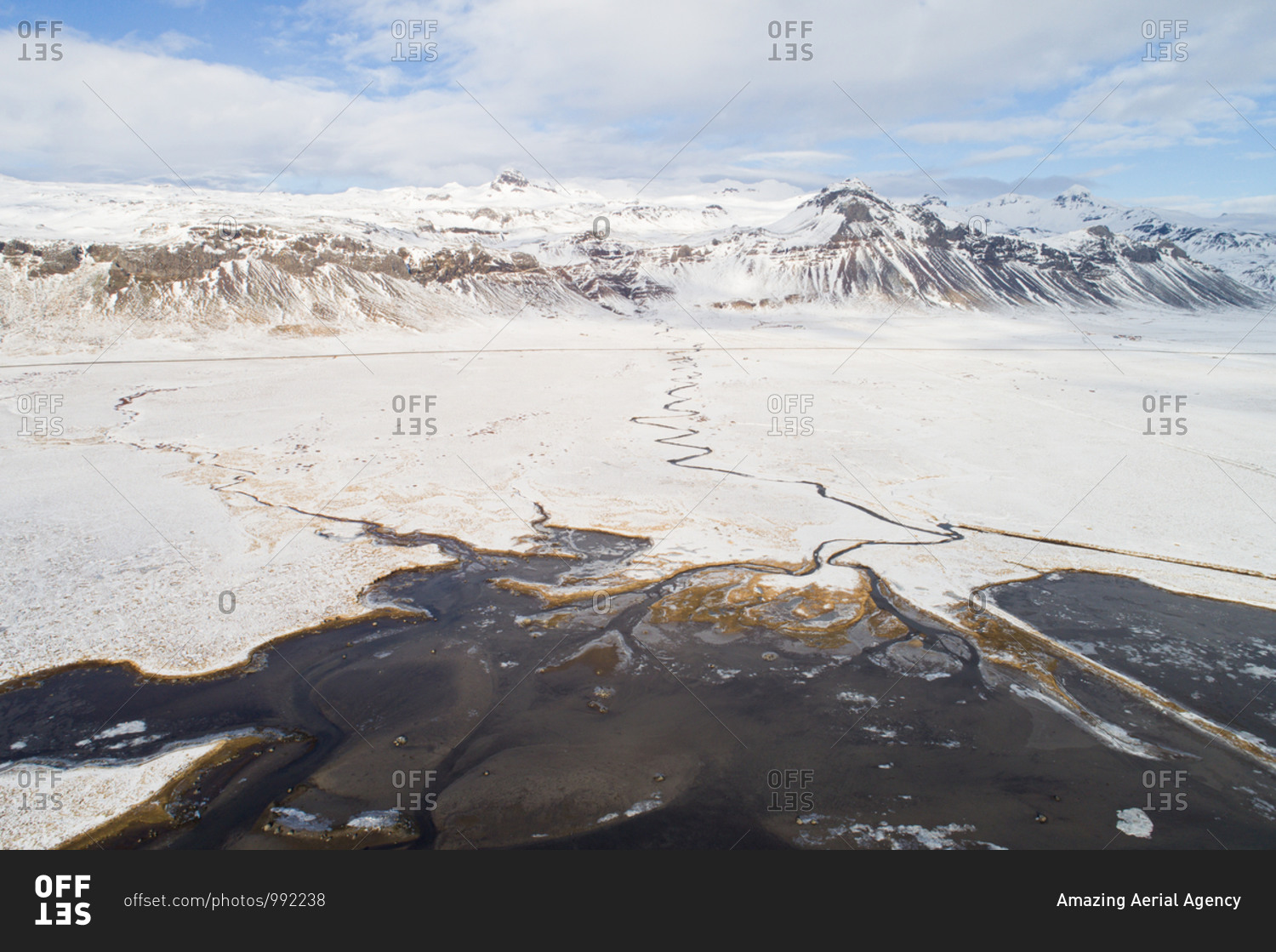 Aerial view of estuary with sandbanks near Budir, in front of snow-covered land and mountains in winter, Snaefellsnes, western Iceland