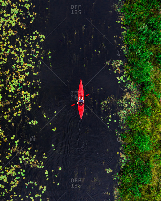 Aerial view of travel person paddling in wild river with red kayak, shot in Labanoras, Lithuania.