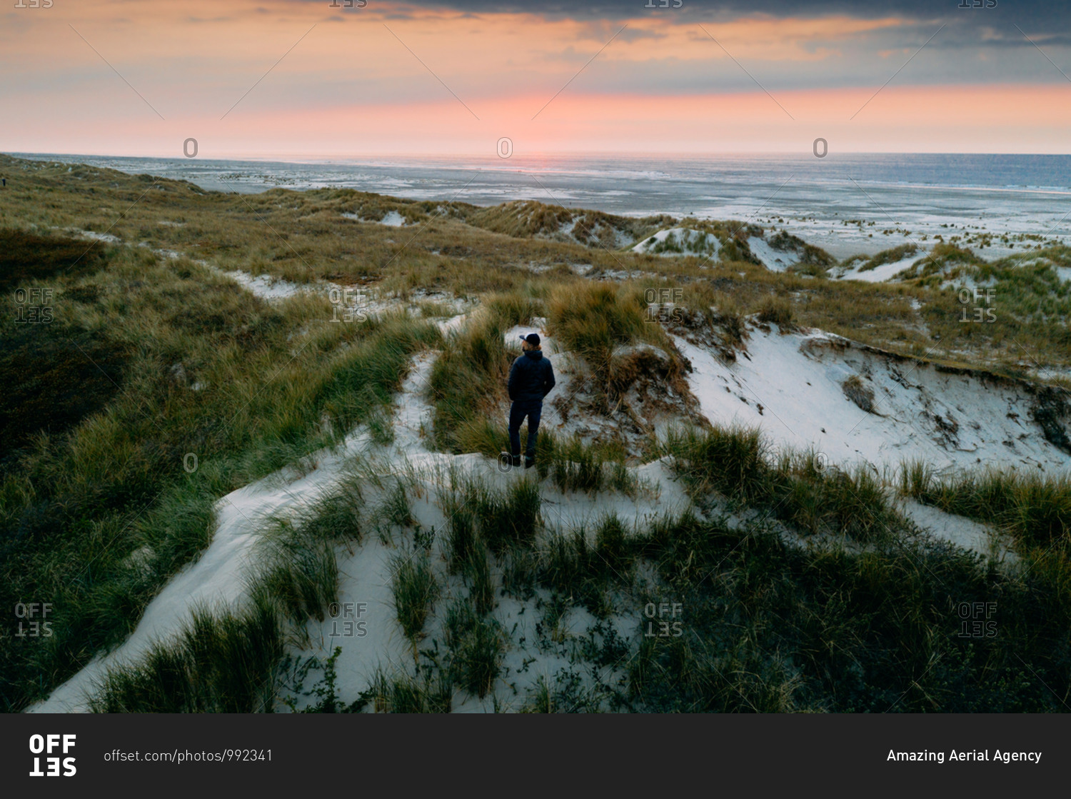 Aerial view of man standing on top of the dunes overlooking the ocean during sunset on the island Terschelling, Friesland, The Netherlands.