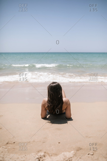Young woman in bikini sitting on the sand looking out to sea