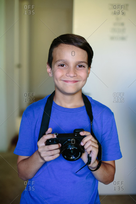 Boy in a blue shirt holds a camera while smiling for a portrait