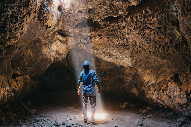 Man admires cascading light beam in lava cave