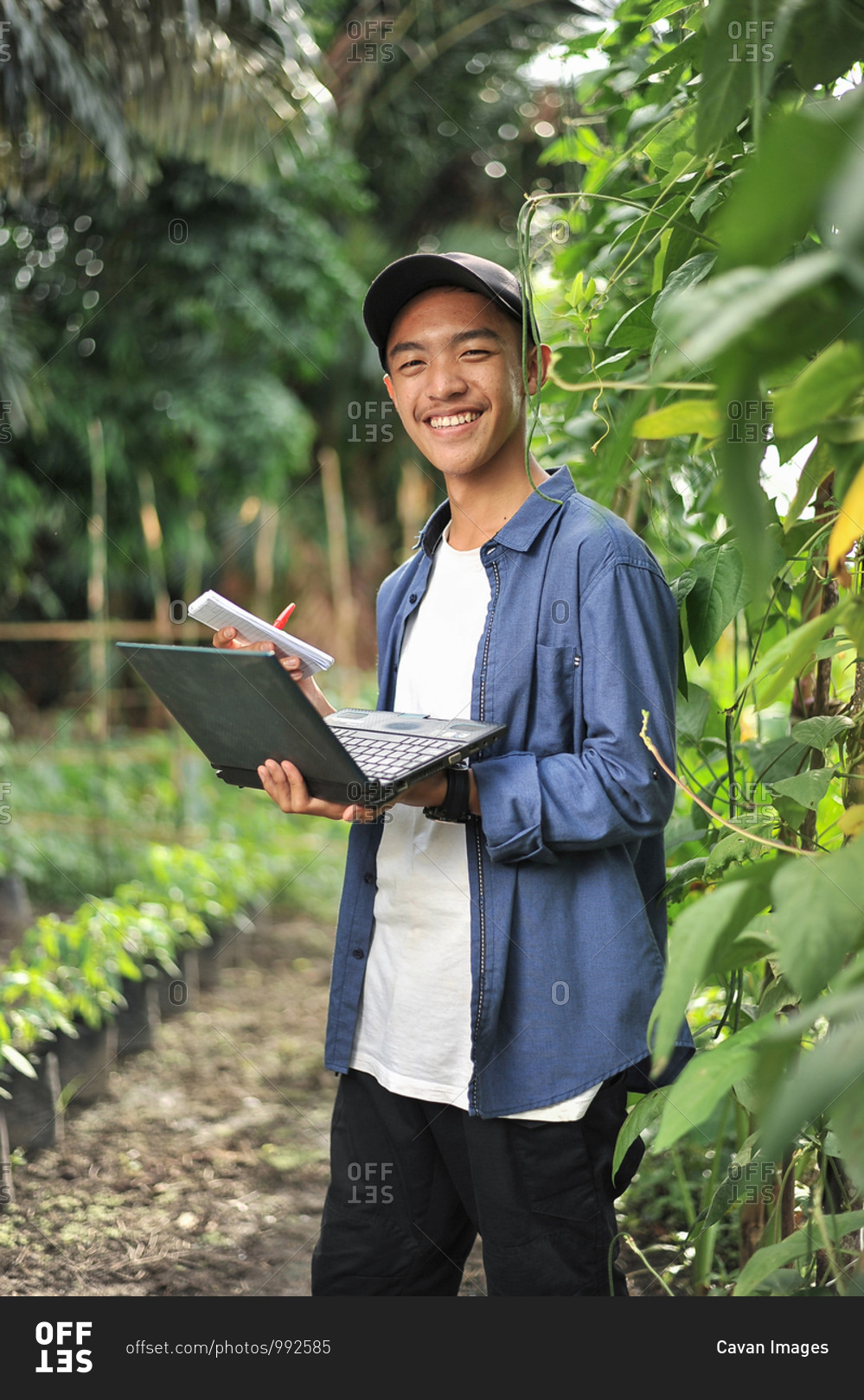 Young Asian farmer man holding laptop at the garden