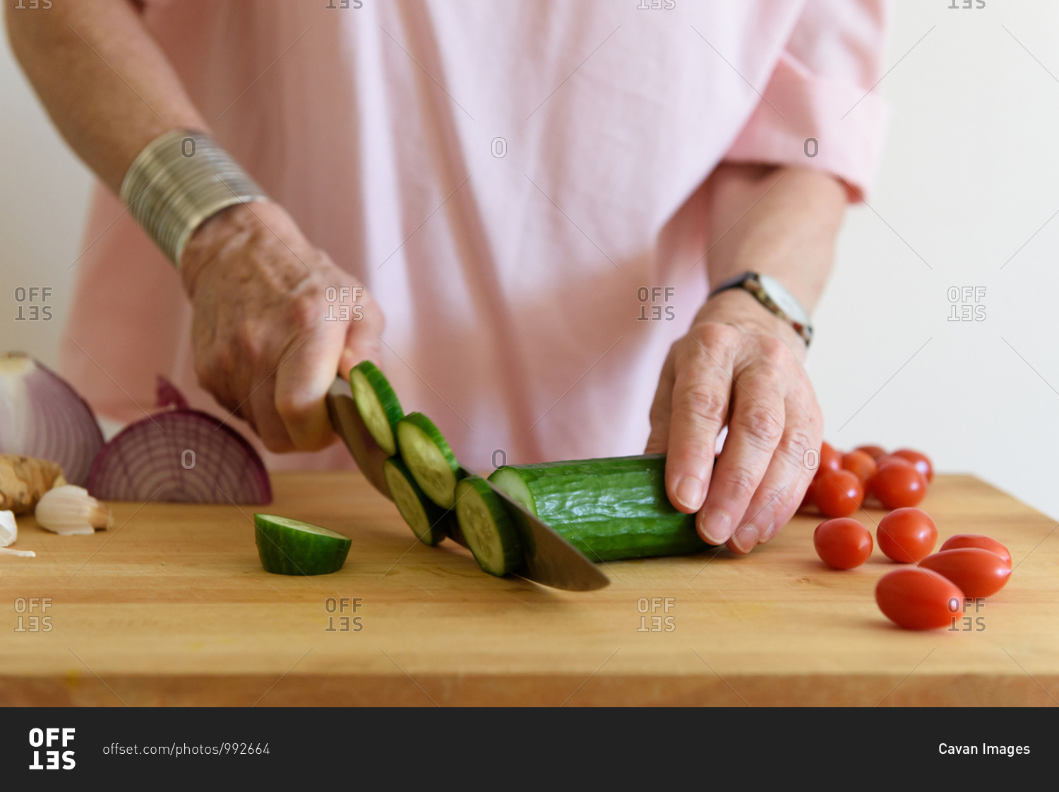 Close up of older woman's hands cutting cucumbers on chopping block