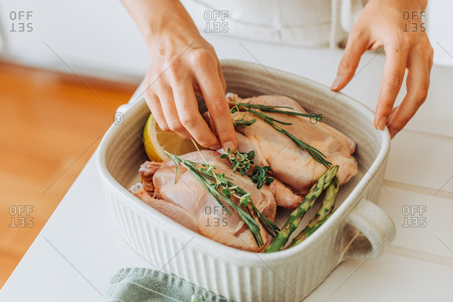 Hands preparing raw quail or chicken with aromatic herbs for roasting