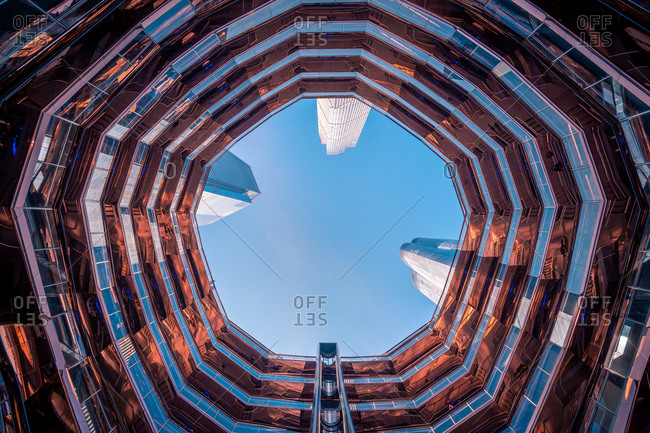 March 7, 2020: Modern skyscrapers seen from inside of Vessel artwork against blue sky in Hudson Yards in New York City