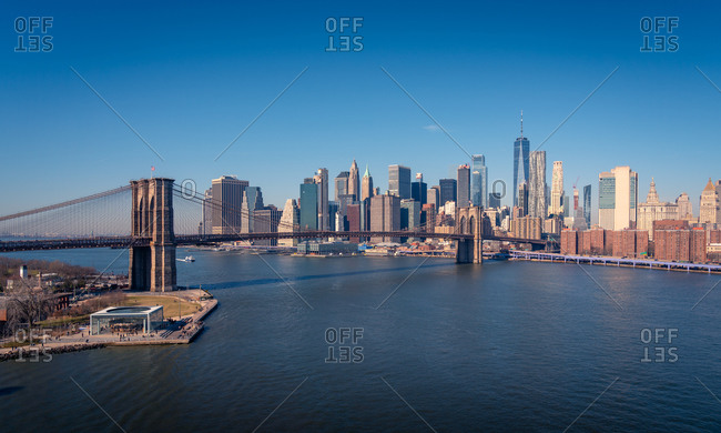 Amazing New York city skyline with famous Brooklyn bridge over river against cloudless blue sky in sunny day