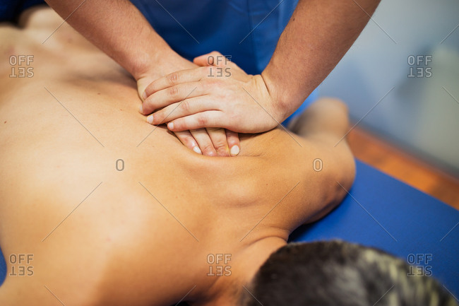 Osteopath in blue uniform examining back of unrecognizable slim male patient with dyed hair lying on examination table in clinic