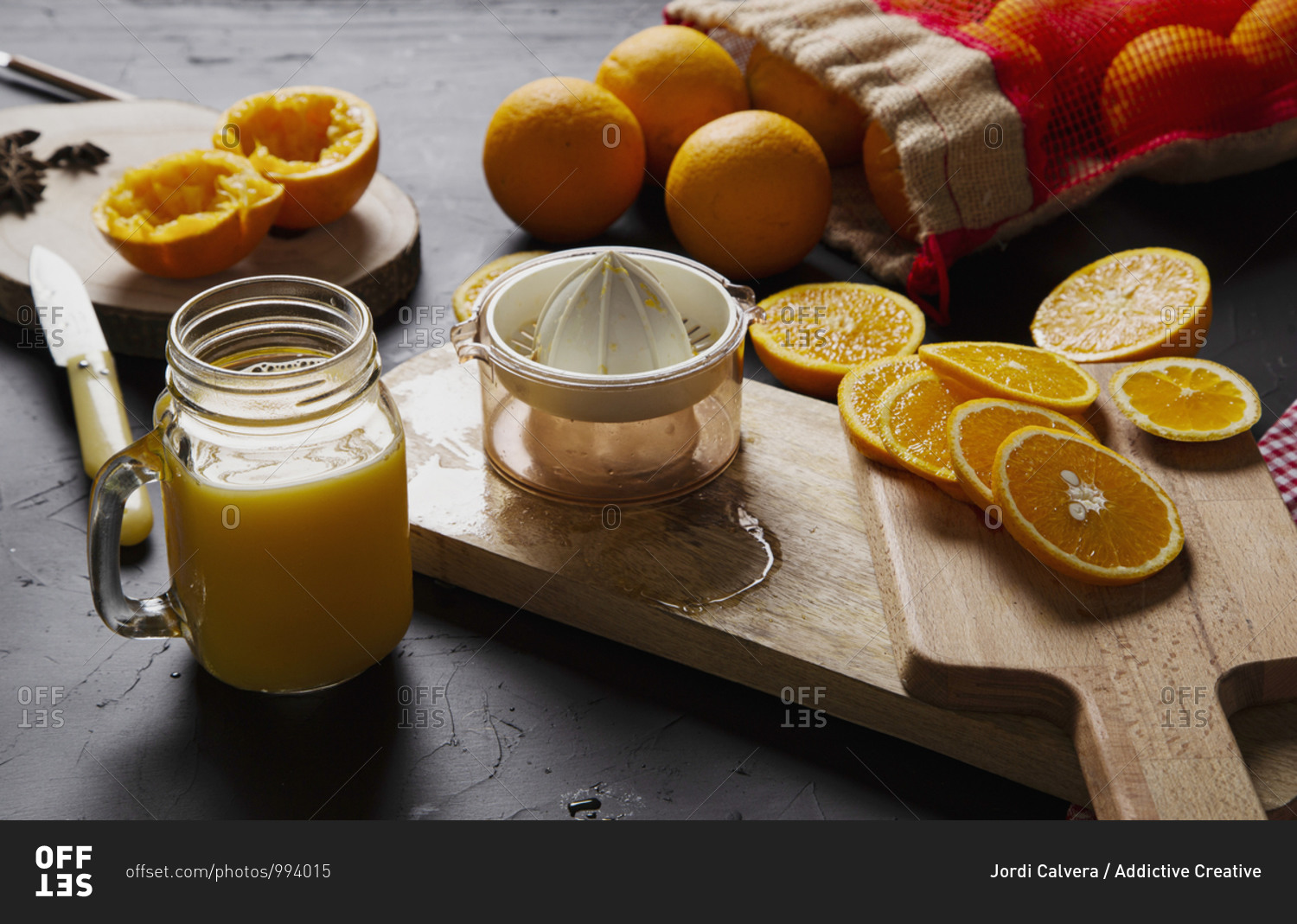 From above composition of halves of fresh oranges on wooden boards and mesh bag near glass jar with orange custard and plastic squeezer
