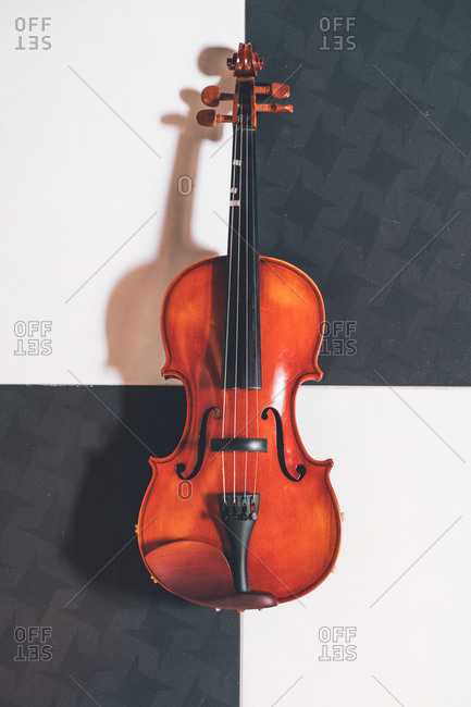 From above of shiny violin with strings placed on chess board pattern floor