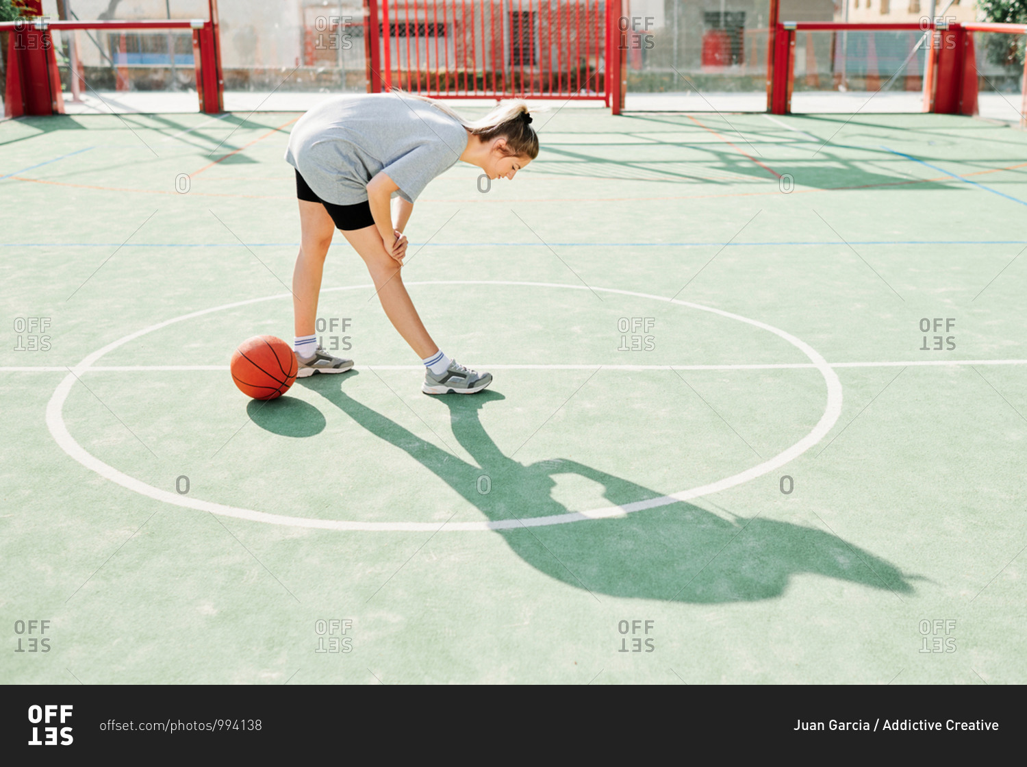 Full body side view of female basketball player performing forward bend exercise while warming up during training on sports ground