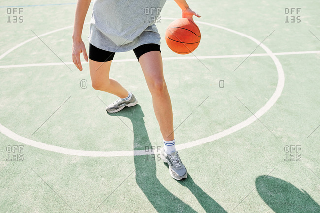 Crop anonymous sporty female practicing dribbling with basketball ball while playing alone on sports ground in sunny day