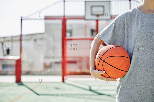 Crop of young sportswoman with basketball ball while standing on court in sunny summer day