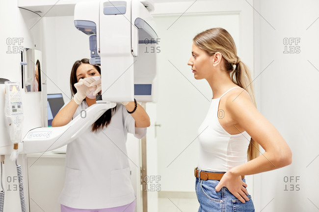 Blond woman with hands on waist waiting for dentist to adjust X ray machine settings during appointment in modern dental clinic
