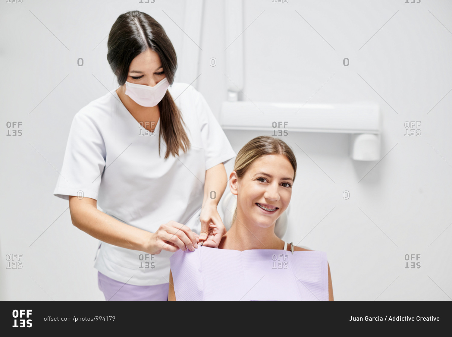 Cheerful female patient smiling and looking at camera while sitting on chair near dentist during visit in modern dental clinic