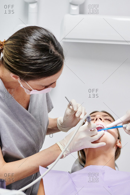 Dental doctor checking teeth of female client wearing braces while using mouth mirror