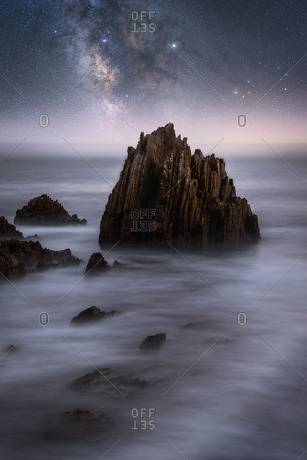 Amazing scenery of sea coast with calm water and rocky cliffs under dark sky with Milky Way