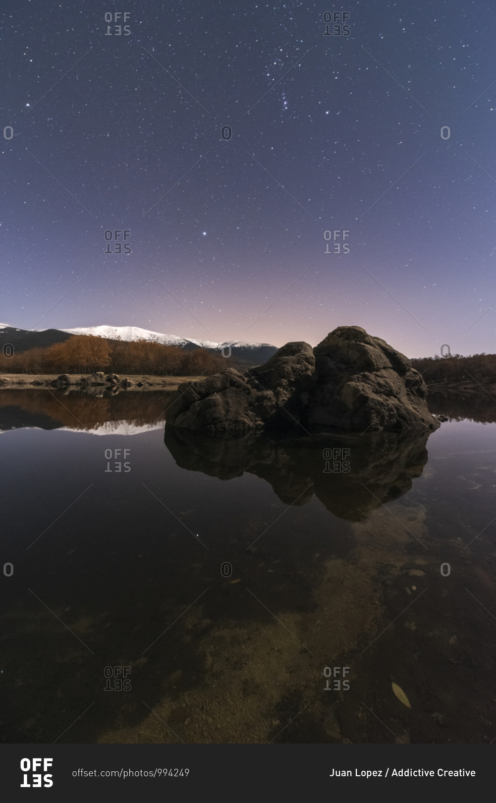Amazing scenery of lake and snow mountains under dark sky with stars and a rock in first plane