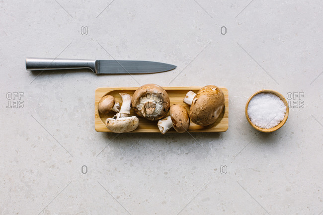 Top view of fresh mushrooms served on wooden plate on table near salt in bowl and a knife