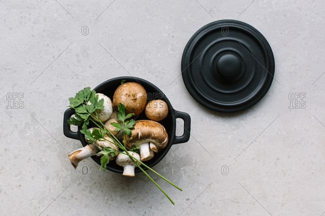 Top view of fresh champignons in saucepan placed on table with salt and parsley in kitchen