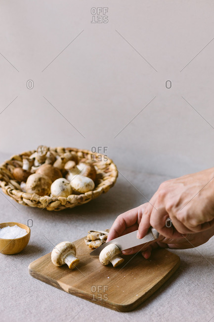 Unrecognizable person chopping raw champignons on wooden cutting board while preparing healthy dish