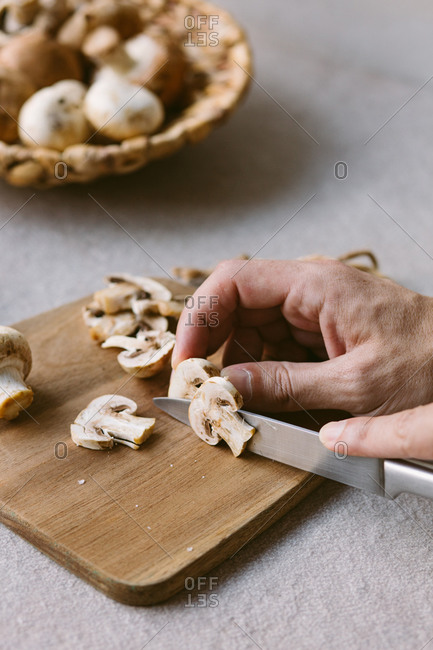 Unrecognizable person chopping raw champignons on wooden cutting board while preparing healthy dish