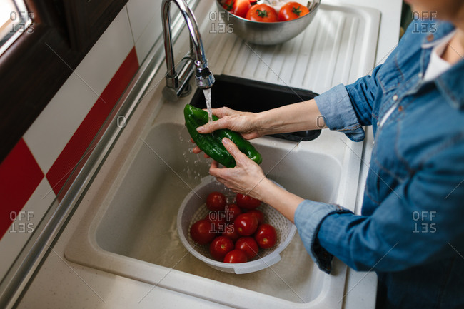 Hands of an unrecognizable person washing vegetables in the sink.